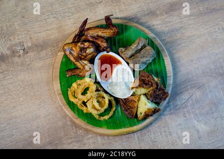 Piatto di cibo composto da ali di pollo affumicato, anelli di cipolla, lekor di keropok o snack di pesce fritto e frittelle di gamberi fritte. Foto Stock