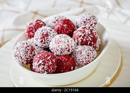 Palline di beatitudine al glutine senza glutine con cocco essiccato e lamponi con semi di chia, more, mirtilli con semi di chia su un recipiente bianco su un bianco Foto Stock