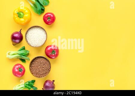 Cornice di diversi alimenti per la salute - grano saraceno, riso, bok choy, peperone giallo, pomodori, lattuga, verde, cetriolo, cipolle su sfondo giallo Top Foto Stock