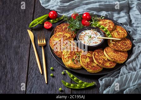 primo piano di piselli verdi e frittelle d'avena su un piatto bianco con salsa semplice di yogurt greco con germogli di piselli e grano freschi, concetto di dieta sana, Foto Stock