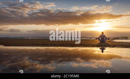 yoga meditazione silhouette lotus alba spiaggia, consapevolezza, benessere e concetto di benessere, riflessione acqua dell'uomo in yoga lotus posa seduta da sola Foto Stock