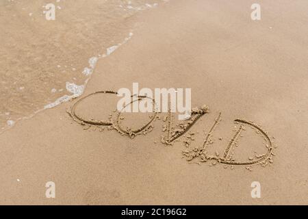 Covid scritto sulla sabbia di una spiaggia con onde di lavaggio, cancellando o cancellando durante l'estate di Coronavirus, Covid libero, FERMATA Covid, spiaggia sicura Foto Stock