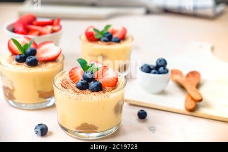 In casa, squisiti dessert Tiramisu' in vetri decorati con fragola, mirtillo, menta bianca sul tavolo di legno, Foto Stock