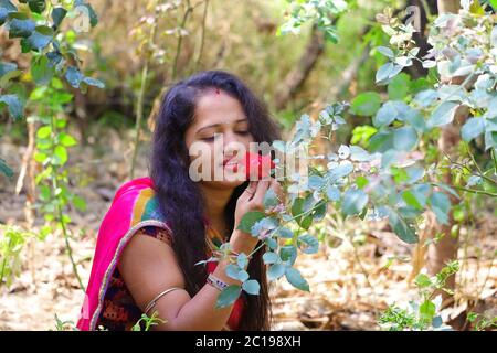 Una giovane ragazza che tiene una rosa in giardino e guardando il fiore rosso di rosa Foto Stock