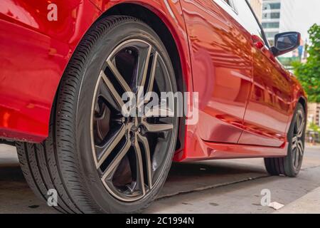 Esterno dell'auto rosso lucido con primo piano delle ruote in gomma nera contro la strada Foto Stock