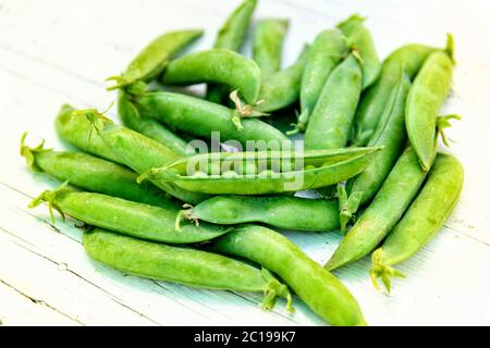 Piselli freschi nel baccello con uno aperto sulla cima del palo per esporre il legume all'interno su un rustico tavolo bianco in un mercato contadino all'aperto in giorno Foto Stock