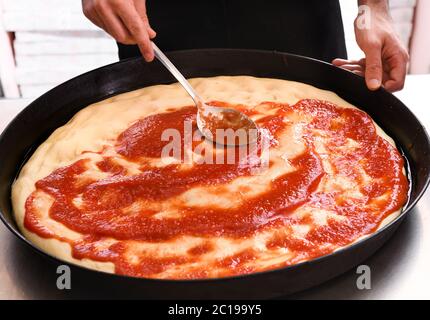 Chef stendendo il pomodoro su una base di pizza in una padella in un ristorante o pizzeria da vicino sulle sue mani Foto Stock