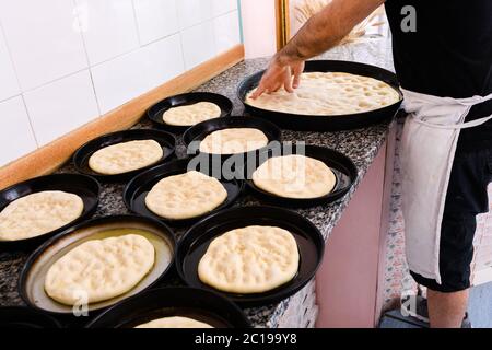 Chef stende porzioni di pasta per pizza in vassoi da forno individuali in una cucina pizzeria durante la preparazione Foto Stock