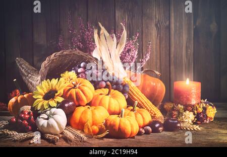 Buon Ringraziamento. Cornucopia decorativa con zucche, zucca, frutta e foglie cadenti su tavola rustica in legno Foto Stock