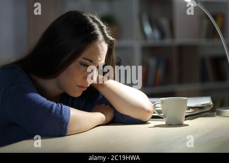 La donna triste si lamenta di sedersi su una scrivania di notte nel soggiorno di casa Foto Stock