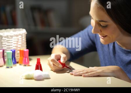 Donna felice dipingendo unghie su un tavolo seduto di notte a casa Foto Stock