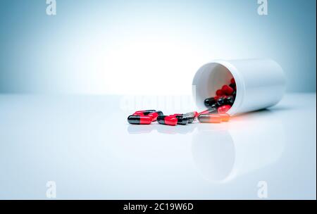 Pillole di capsula di antibiotico rosso-nero sparso fuori del flacone di droga di plastica su sfondo bianco. Industria farmaceutica. Resistenza agli antibiotici. Foto Stock