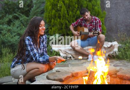 Giovane coppia con chitarra vicino al fuoco all'aperto Foto Stock