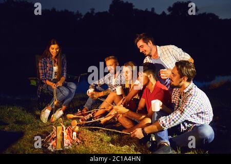 Un gruppo di persone sedute da falò accanto alla tenda di notte in estate in autunno. Foto Stock