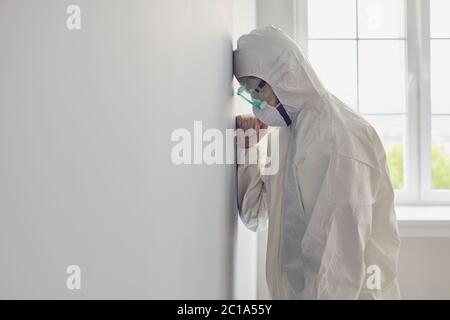 Medico stanco in indumenti protettivi in piedi in ospedale. Duro lavoro degli operatori medici durante un'epidemia di virus Foto Stock