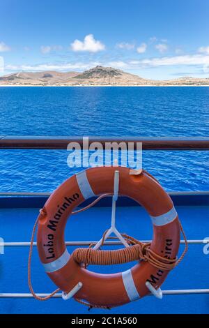 Vista della vetta 'Pico Ana Ferreira' dalla barca 'Lobo Marinho' con scritto 'Lobo Marinho' in lifebuoy come primo piano nell'isola di Porto Santo, in Portogallo Foto Stock