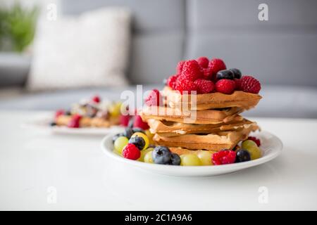 Dolce ragazzo di compleanno del bambino, mangiando waffle belgi con lamponi, mirtilli, cocnoci e cioccolato a casa