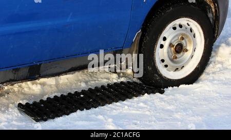 il tappetino antiscivolo nero di forma rettangolare è posto sotto la ruota di un'auto a basso livello dopo essere rimasto bloccato in una deriva da neve e s. Foto Stock