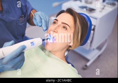Medico dentista che usa apparecchiature leggere di cura dentale per riempire, esaminare i denti di un paziente in studio di odontoiatria. Stomatologia e concetto di assistenza sanitaria Foto Stock