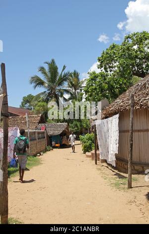 Tovaglie in vendita appese in vendita sul marciapiede, e due pedoni maschi, Ampangorinana Village, Isola di Nosy Komba, Madagascar. Foto Stock