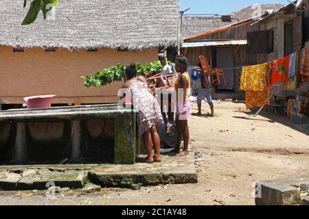 Ragazze che lavano i vestiti con i secchi e li asciugano sulla linea di lavaggio, Villaggio di Ampangorinana, Isola di Nosy Komba, Madagascar. Foto Stock