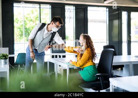 Giovani con maschere di fronte al lavoro in ufficio dopo blocco, saluto. Foto Stock