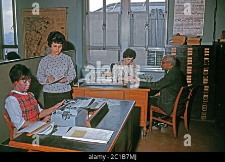 Lavoro di ufficio come era negli anni '60 – qui al Rikers Island carcere complesso, East River, New York, USA 1963. Quattro persone sono in questo spazio di lavoro: Due persone bianche e due nere. Una donna prende appunti e vecchie macchine da scrivere manuali sono in uso. Foto Stock