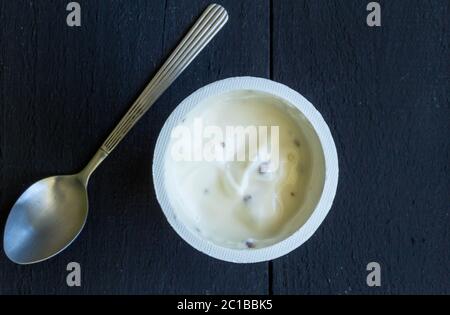 Yogurt in tazza di plastica primo piano su tavolo nero. Foto dall'alto di yogurt alla vaniglia a scaglie di choc con argento Foto Stock