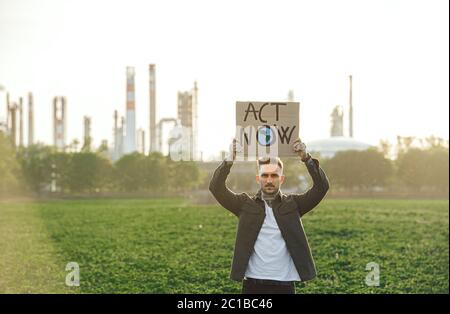 Giovane attivista con placche in piedi all'aperto da raffineria di petrolio, protestando. Foto Stock