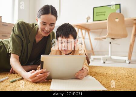 Ritratto di giovane madre sorridente che si posa sul pavimento con il figlio carino utilizzando tablet difitale, spazio di copia Foto Stock