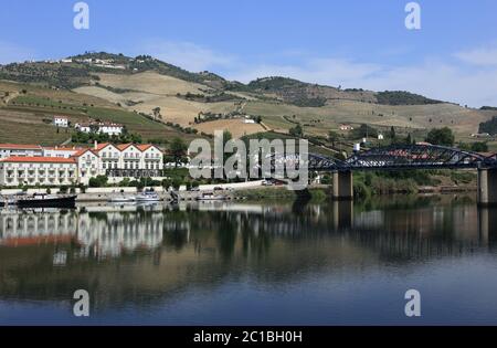 Portogallo, Regione del Douro, Pinhao. Vista panoramica di Pinhao e del suo ponte in acciaio sul fiume Douro che si riflette sull'acqua. Sito patrimonio dell'umanità dell'UNESCO. Foto Stock