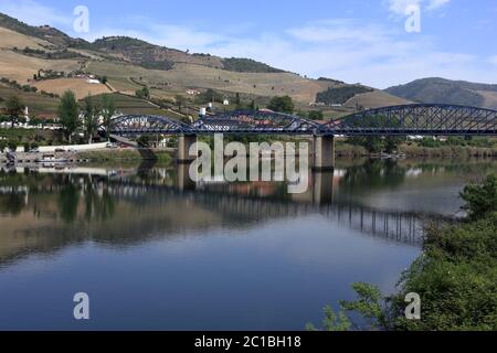 Portogallo, Regione del Douro, Pinhao. Vista panoramica di Pinhao e del suo ponte in acciaio sul fiume Douro che si riflette sull'acqua. Sito patrimonio dell'umanità dell'UNESCO. Foto Stock