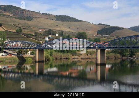 Portogallo, Regione del Douro, Pinhao. Vista panoramica di Pinhao e del suo ponte in acciaio sul fiume Douro che si riflette sull'acqua. Sito patrimonio dell'umanità dell'UNESCO. Foto Stock