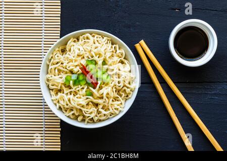 Ciotola di tagliatelle semplici, cucinate in istante, con bastoncini di bambù e guarnitura di pepe verde e rosso - Top v Foto Stock