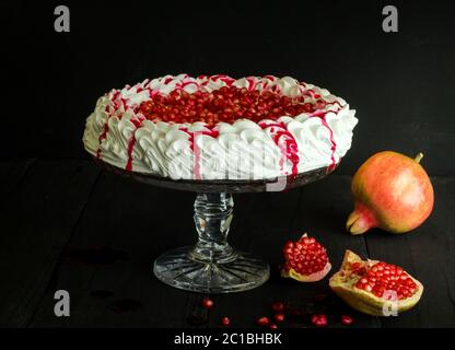 Torta di meringa fatta in casa Pavlova , semi di melograno fresco e salsa su torta vintage stand su wo nero Foto Stock