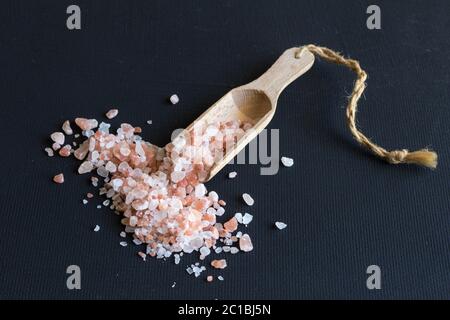 Himalayan rock salt e scoop di legno vicino sul nero sfondo rustico Foto Stock