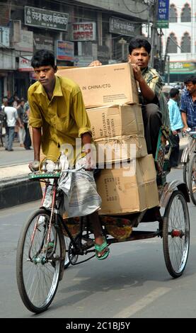 Un uomo in bicicletta un risciò lungo la strada a Dhaka, Bangladesh trasportando scatole e un passeggero. Tipica scena di vita locale a Dhaka, la capitale Foto Stock