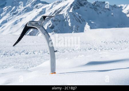 Primo piano di un'ascia ghiacciata nella neve con montagne innevate sullo sfondo Foto Stock