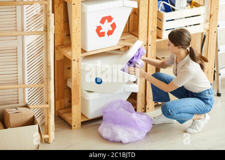 Giovane donna che smista la spazzatura nei pacchetti e poi li getta fuori nei bidoni della spazzatura Foto Stock