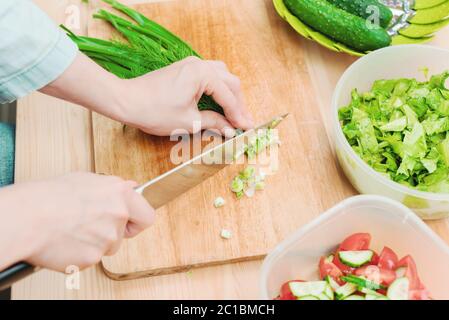 Primo piano di mani femminili delicato affettare sulla tavola di legno i gambi di cipolle verdi facendo insalata. Il concetto di un h vegetariano Foto Stock