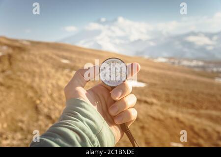 una mano dell'uomo tiene una bussola a mano sullo sfondo di montagne e colline al tramonto. Il concetto di viaggio e navigati Foto Stock