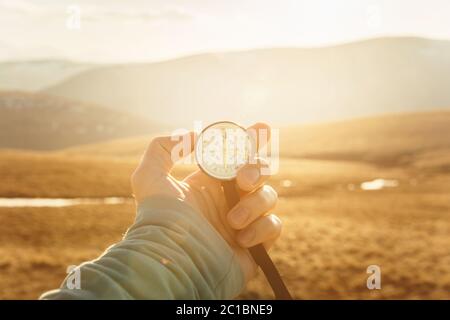 una mano dell'uomo tiene una bussola a mano sullo sfondo di montagne e colline al tramonto. Il concetto di viaggio e navigati Foto Stock