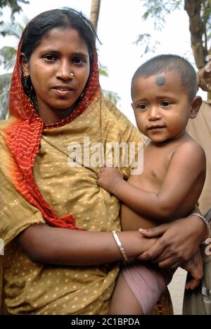 Khulna in Bangladesh. Donna in abiti tradizionali che tiene un bambino. Vita locale a Khulna. Foto Stock