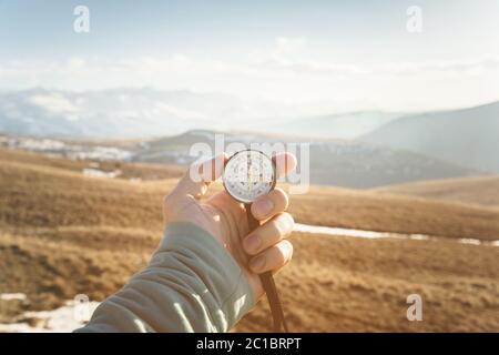 una mano dell'uomo tiene una bussola a mano sullo sfondo di montagne e colline al tramonto. Il concetto di viaggio e navigati Foto Stock