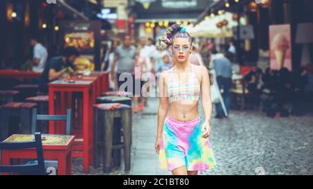 Ragazza giovane funky fresca con capelli pazzi che camminano sulle strade della città godendo le vibrazioni del fine settimana Foto Stock