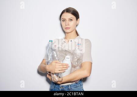 Ritratto di giovane donna che tiene in mano bottiglie di plastica vuote mentre si trova in piedi contro lo sfondo bianco Foto Stock