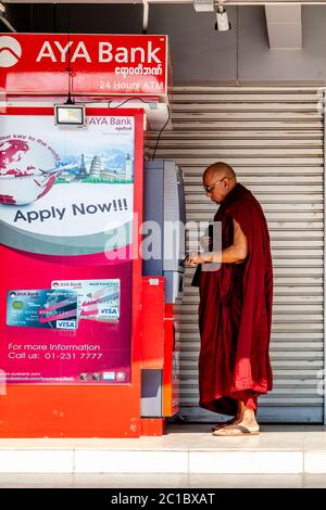 Un monaco buddista ritira denaro da UNA macchina per il cashpoint, Yangon, Myanmar. Foto Stock