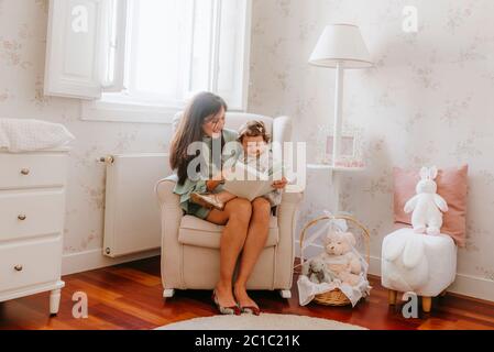 bambina che si diverte a sedere sulla sua madre incinta in camera Foto Stock