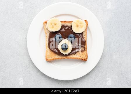 Colazione o pranzo per bambini toast a forma di orsacchiotto, cibo, arte. Panino bianco con crema di nocciole al cioccolato e frutta, menu di cibo per bambini. Isolare Foto Stock