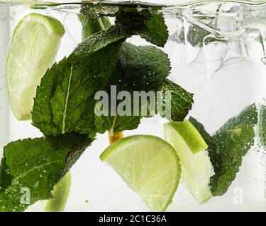 Primo piano vista della limonata fresca e fredda con fette di lime, cubetti di ghiaccio e foglie di menta. Consistenza della bevanda estiva rinfrescante con le macro bolle sul vetro. Spianatura o flottazione fino alla parte superiore della superficie. Foto Stock